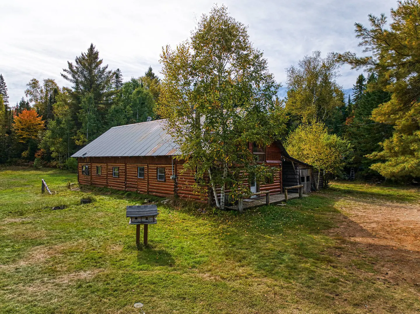 Exterior view of a log cabin with a metal roof, surrounded by green grass and trees.