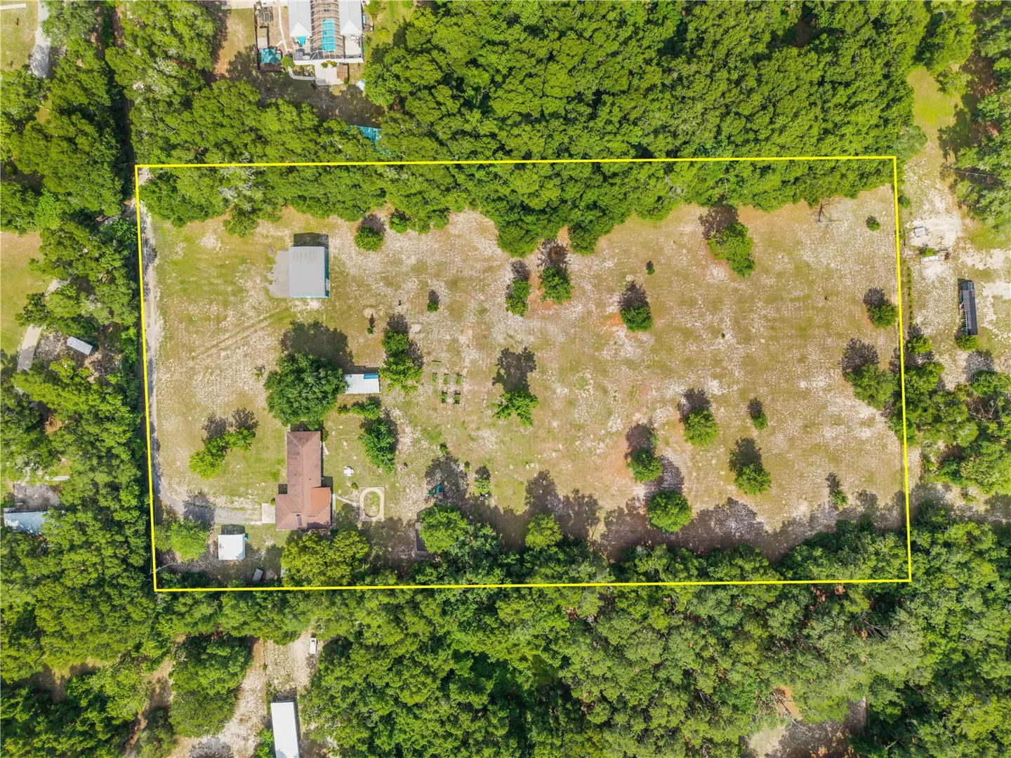Aerial view of a large, rectangular plot of land outlined in yellow, featuring a house, outbuildings, and scattered trees.