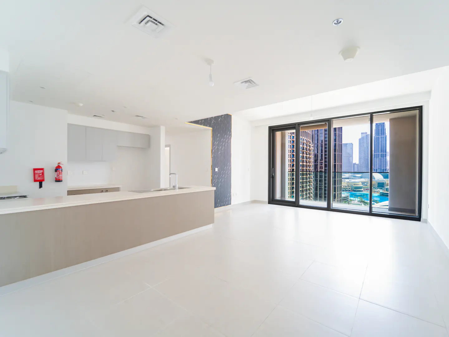Bright, empty apartment with white tile floors, a kitchen island, and a large sliding glass door with a city view.