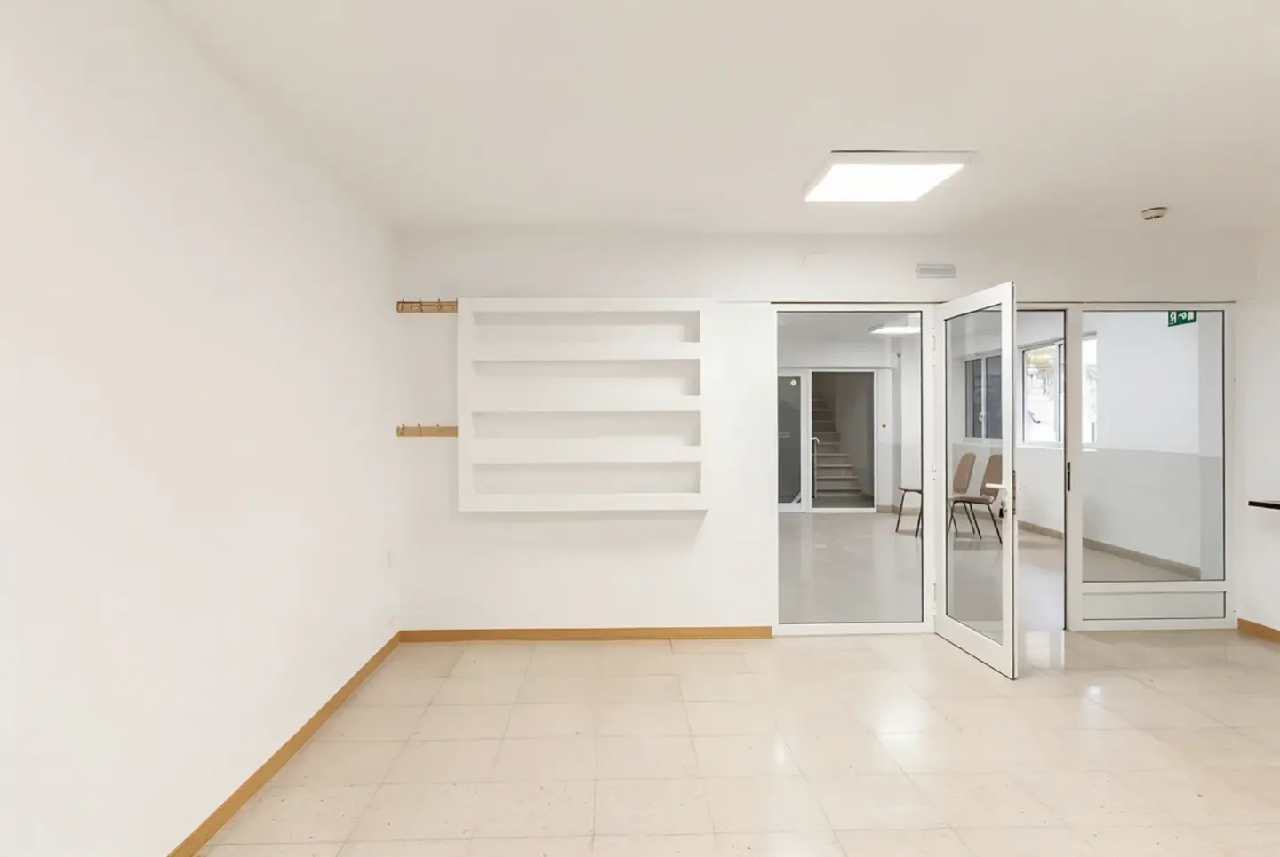 Bright, empty room with white walls, tile floor, and open glass doors. A built-in shelf and coat hooks are on the left wall.