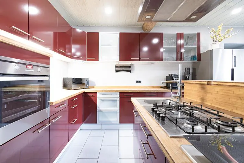 A modern kitchen with red cabinets, stainless steel appliances, and light wood countertops.