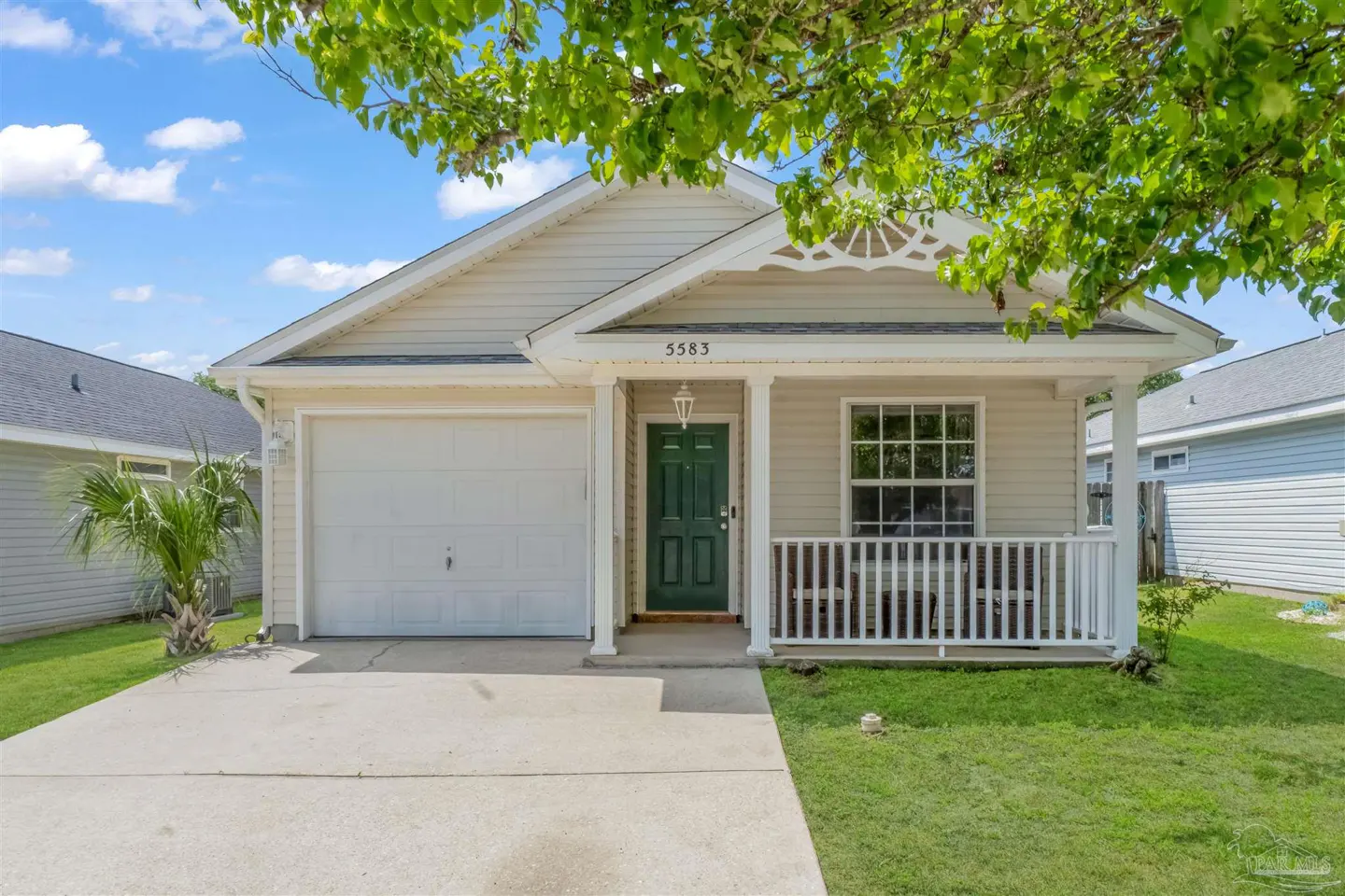 Beige single-story house with a green front door, white garage door, and a small porch with white railings.