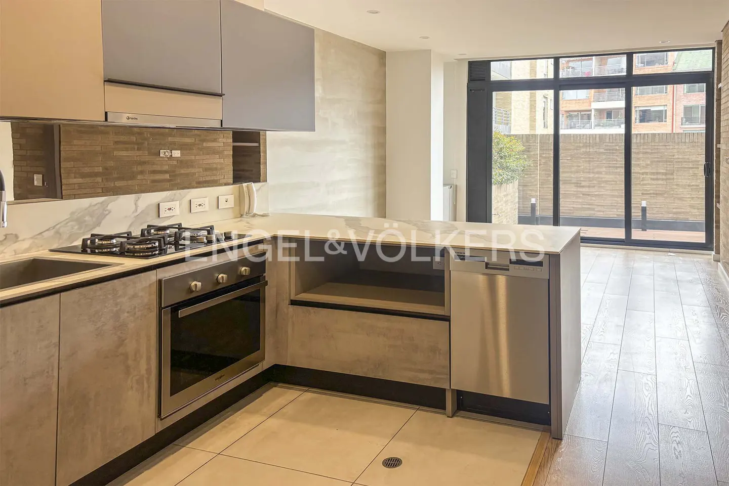 A modern kitchen with gray cabinets, stainless steel appliances, and a large window overlooking a brick courtyard.