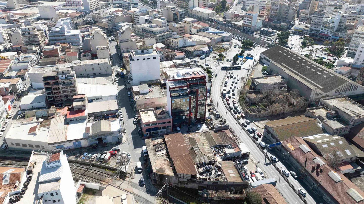 Aerial view of a dense city neighborhood with a mix of modern buildings, older structures, and a busy road with traffic.