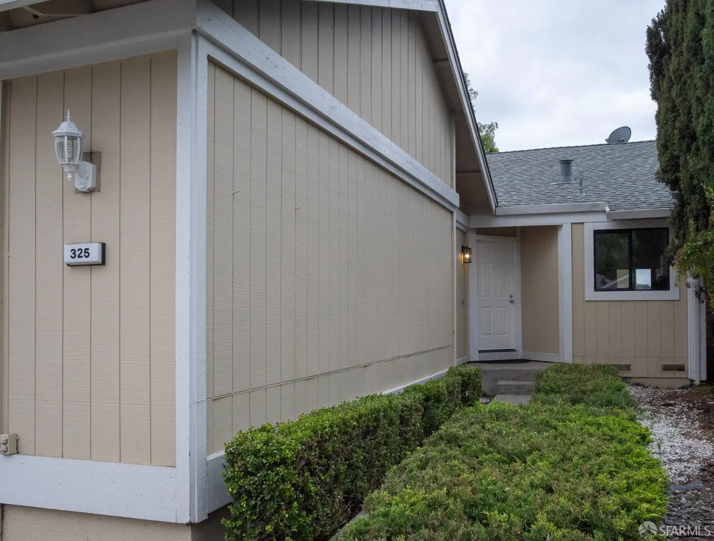 Beige house exterior with white trim, a white front door, and green bushes. Address number 325 is visible.