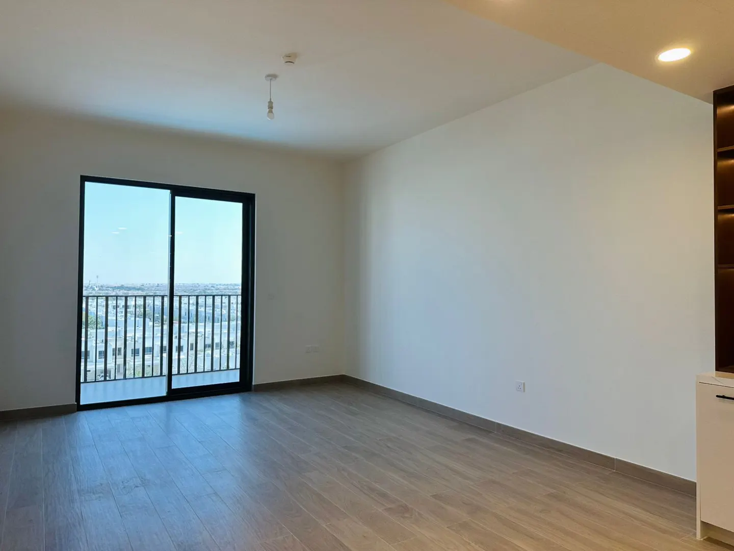 Empty room with wood floors, white walls, and a black-framed sliding glass door to a balcony with a city view.