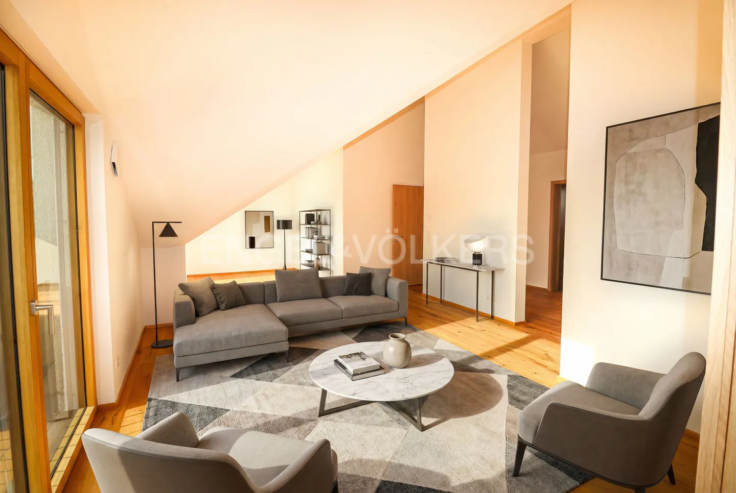 Bright living room with gray sectional, chairs, and geometric rug. A marble table sits in the center. Artwork adorns the walls.