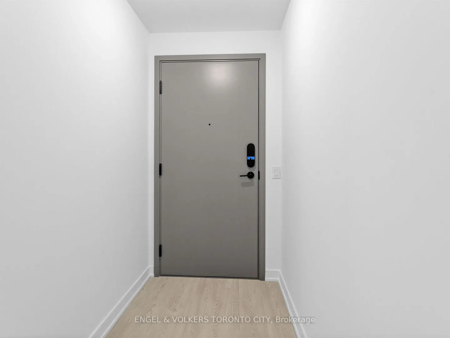 Interior shot of a gray door with a smart lock in a white hallway with light wood floors.