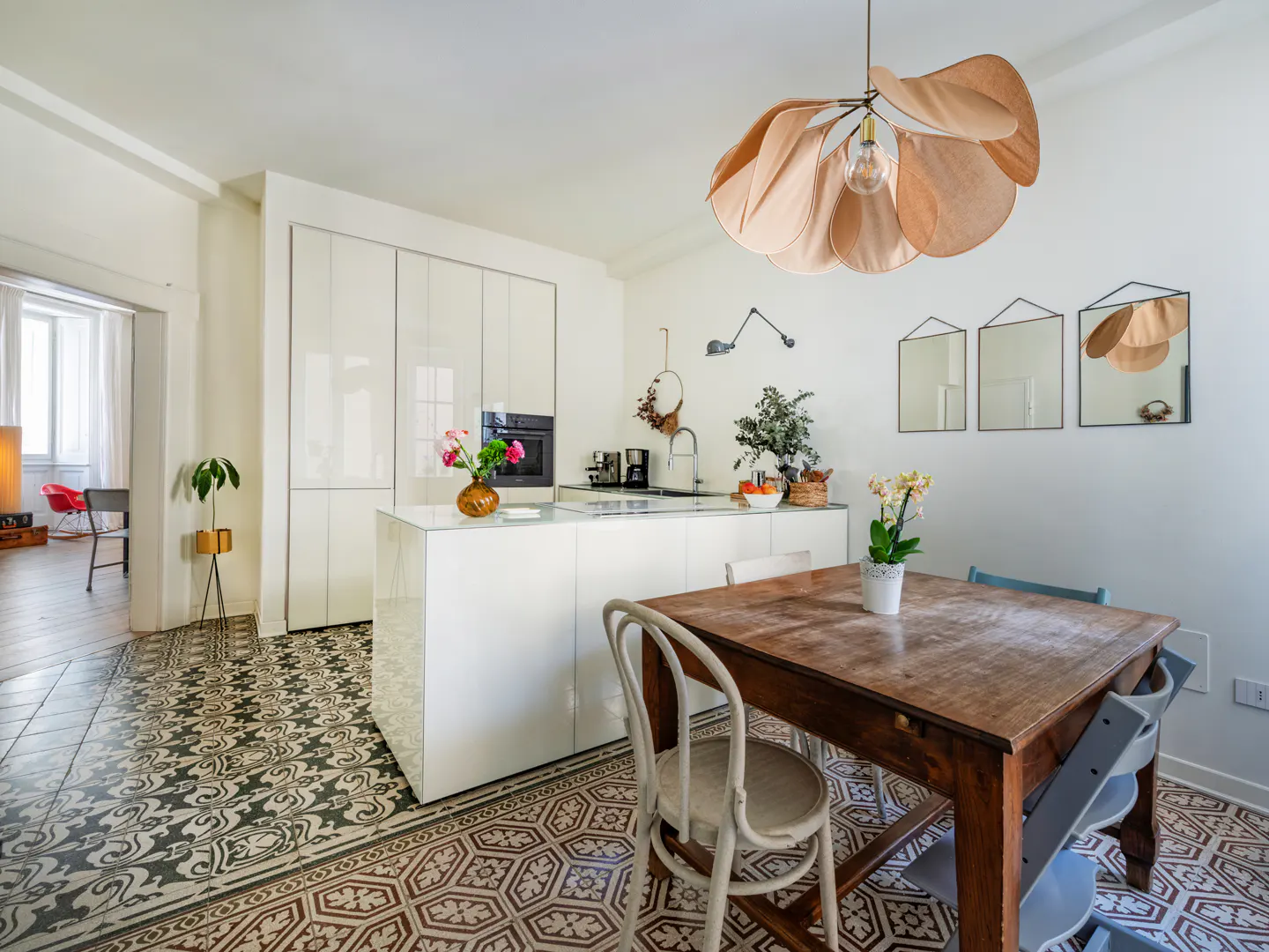 Modern kitchen with white cabinets, a wooden dining table, patterned tile floors, and a unique petal-shaped pendant light.