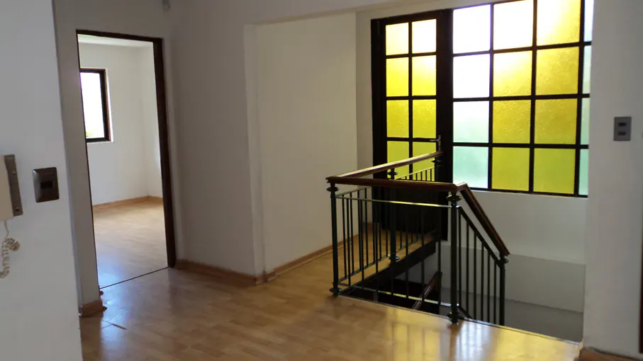 Interior view of a home featuring a staircase with dark metal railings, a large window with yellow and green panes, and a doorway leading to another room.