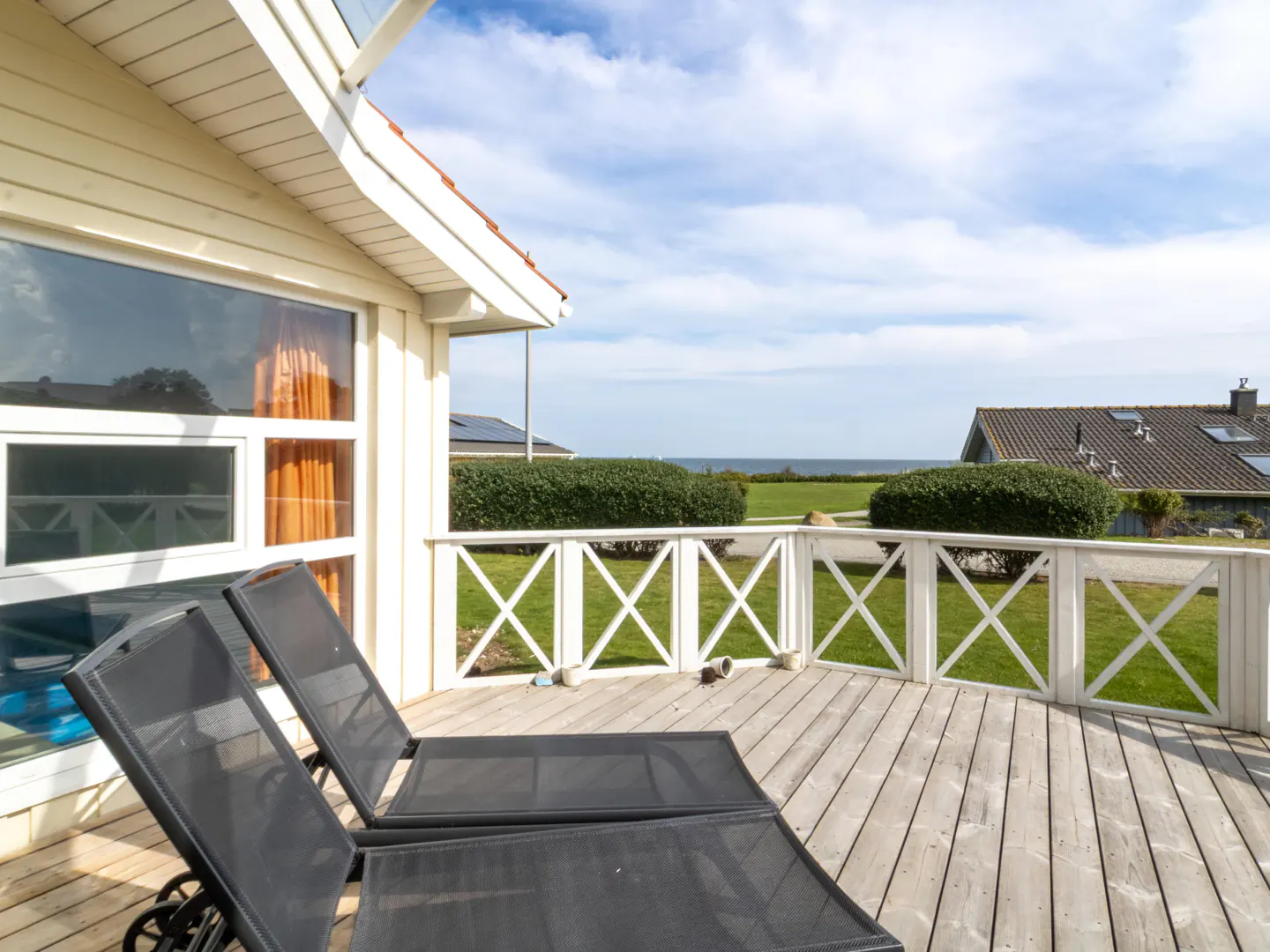 Wooden deck with two black lounge chairs, white railing, and view of the ocean and blue sky.