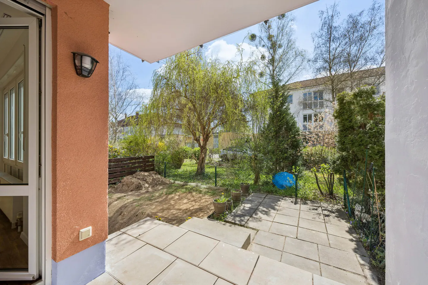 View from a patio with stone tiles, looking out to a green yard with trees and a building in the background.