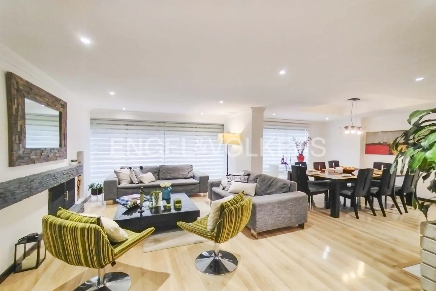 Open-concept living and dining area with wood floors, gray sofas, striped chairs, and a dining table with black chairs.