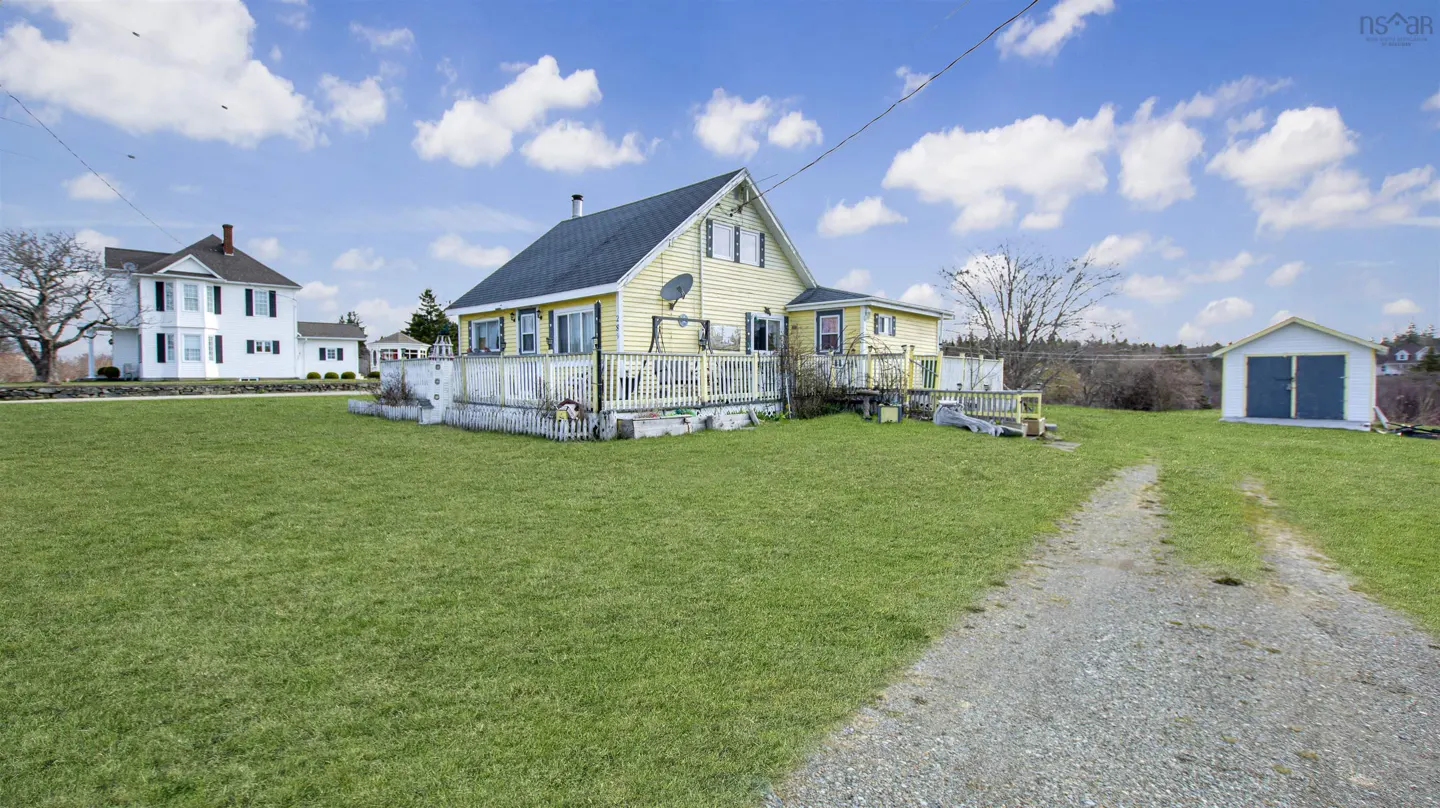 A yellow house with a white porch sits on a green lawn under a blue sky with white clouds.