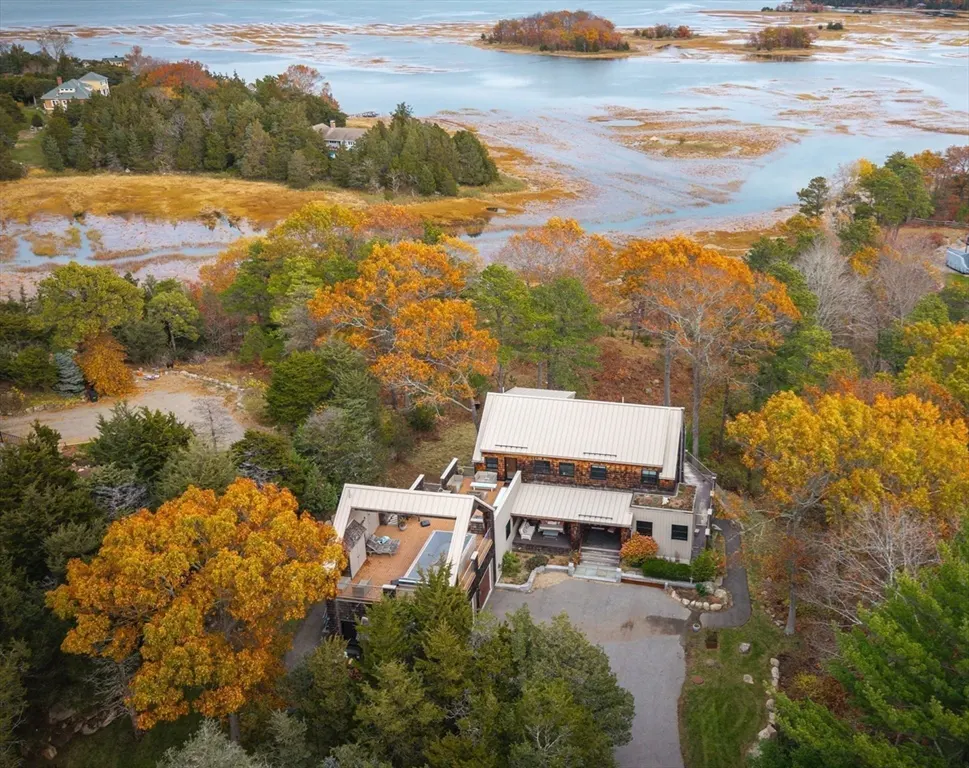 Aerial view of a modern home with a metal roof surrounded by colorful fall foliage near a bay.
