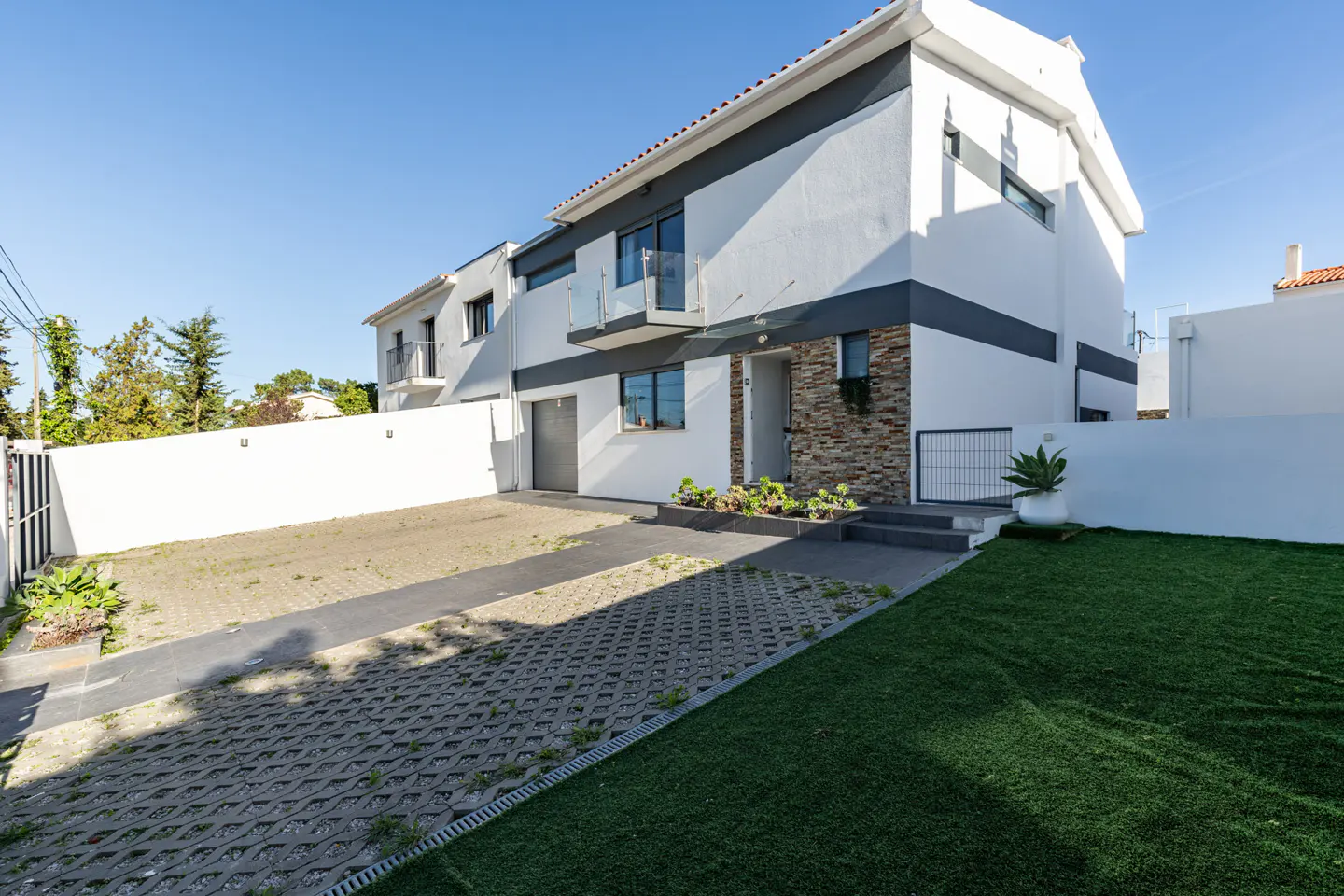 Two-story white house with gray trim, a small balcony, and a stone accent wall. A driveway and lawn are in front.