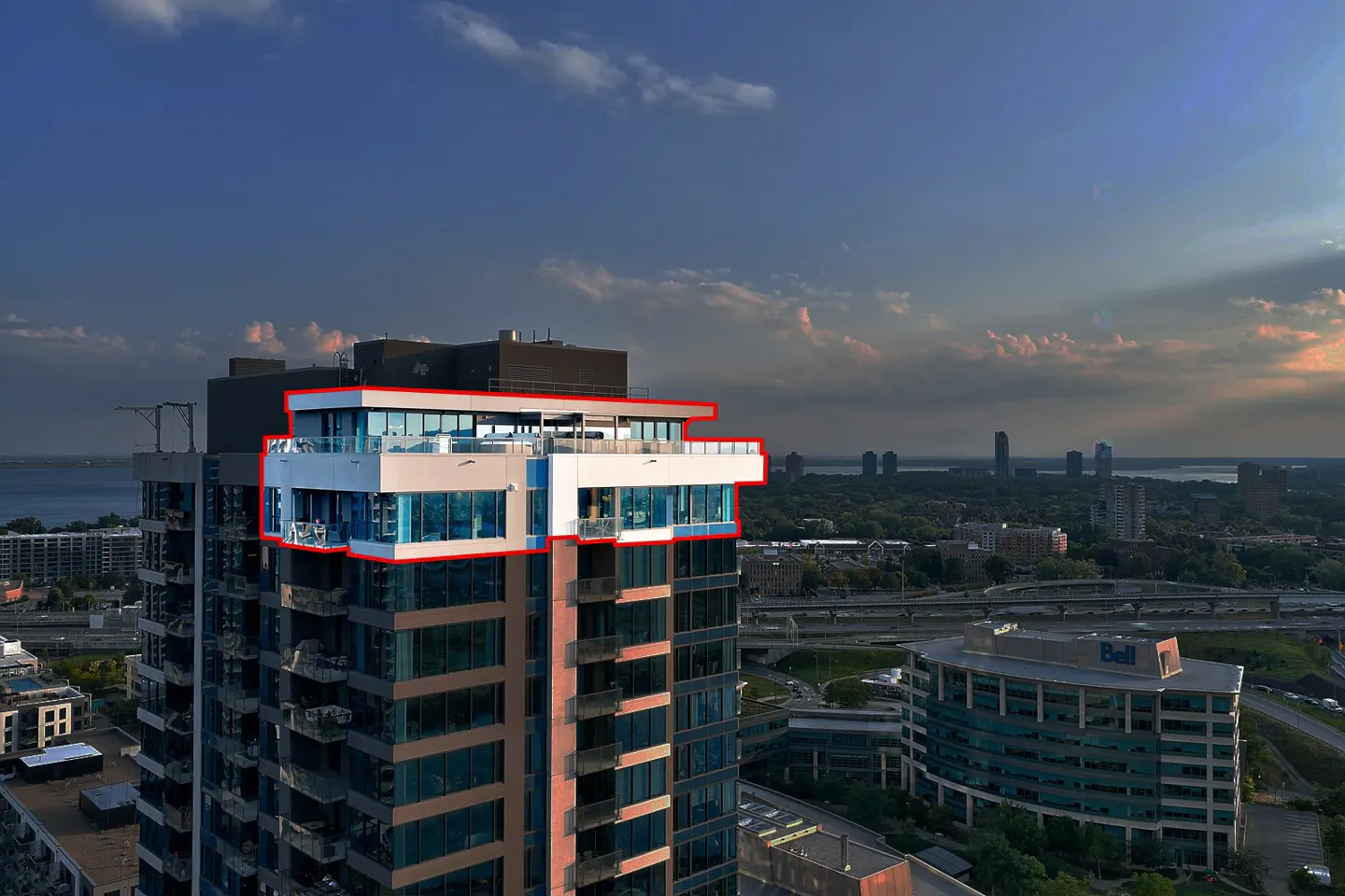 Aerial view of a modern high-rise condo with a glass-enclosed penthouse suite, set against a cityscape and cloudy sky.