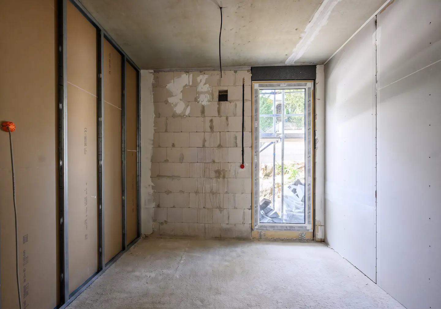 Interior view of a room under construction with block walls, drywall, and a window.