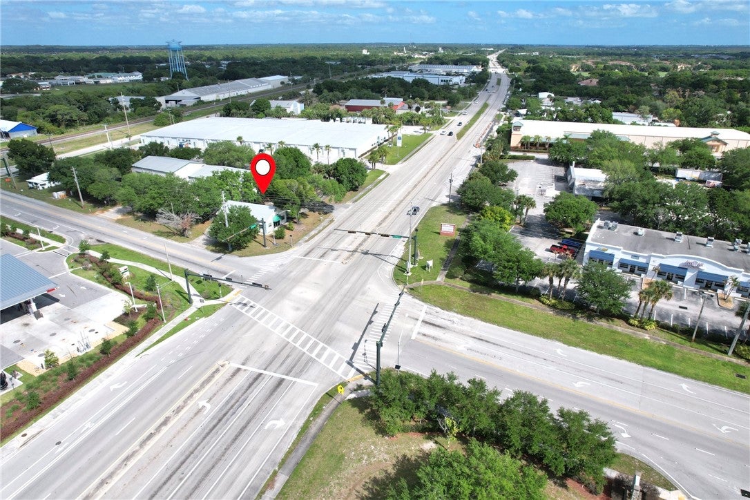 Aerial view of a commercial intersection with a red map pin marking a specific property surrounded by trees and roads.