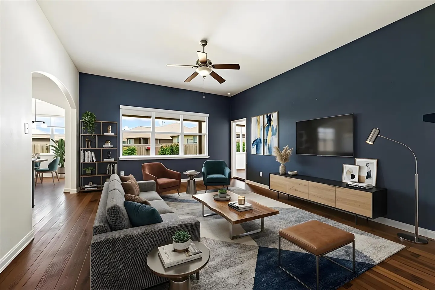Living room with dark blue walls, wood floors, gray sofa, and a ceiling fan. A TV hangs above a light wood console table.