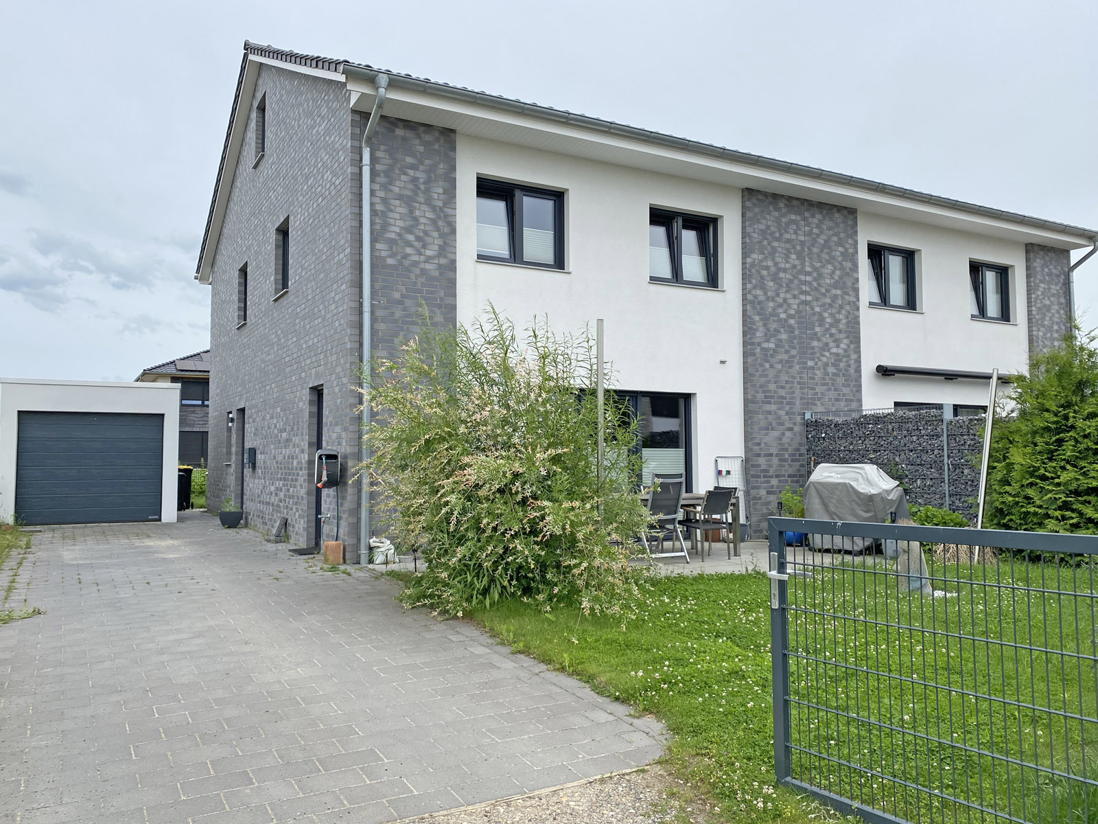 Modern two-story house with grey brick and white facade, paved driveway, detached garage, and a small backyard with patio.