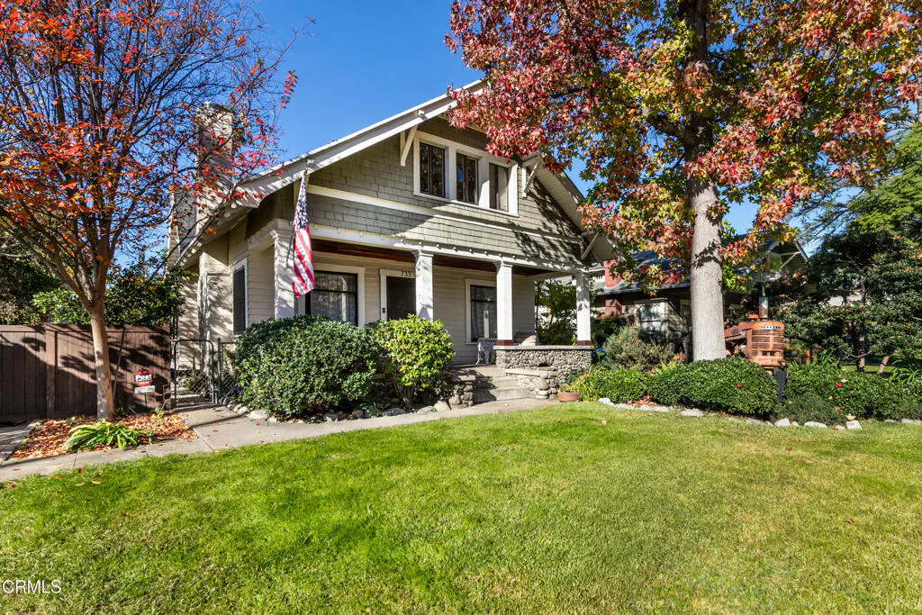 Two-story house with a green lawn, trees with red leaves, and an American flag on the porch.