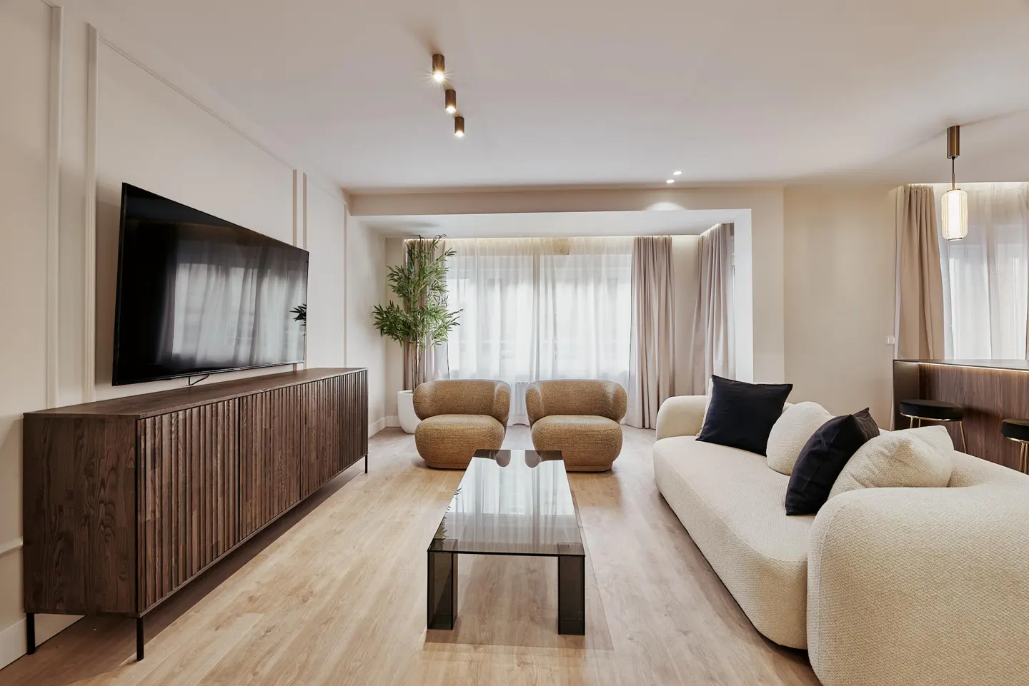 Living room with a large TV on a wooden cabinet, two tan chairs, a white sofa, and a glass coffee table.