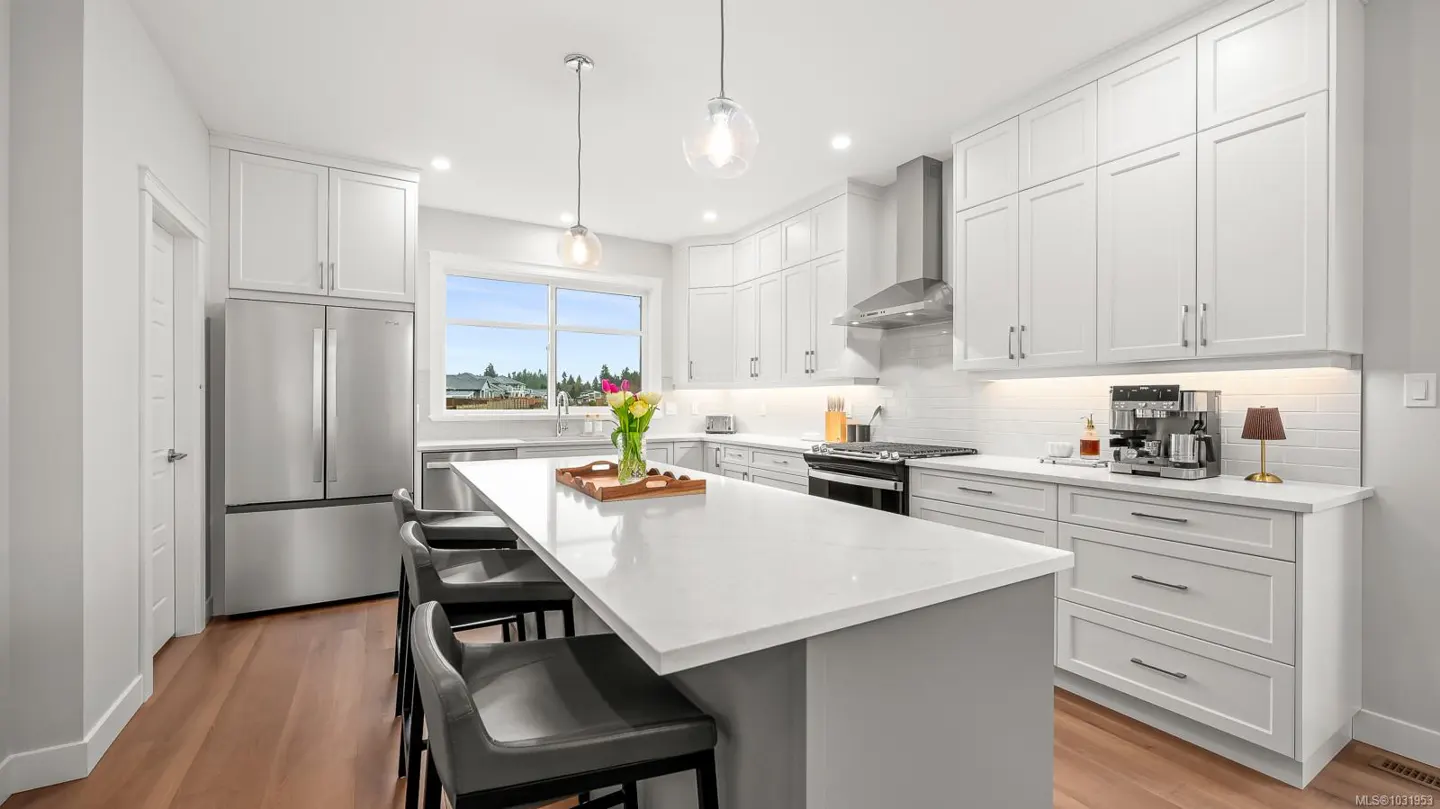 Bright, modern kitchen with white cabinets, stainless steel appliances, and a large island with seating. Hardwood floors add warmth.