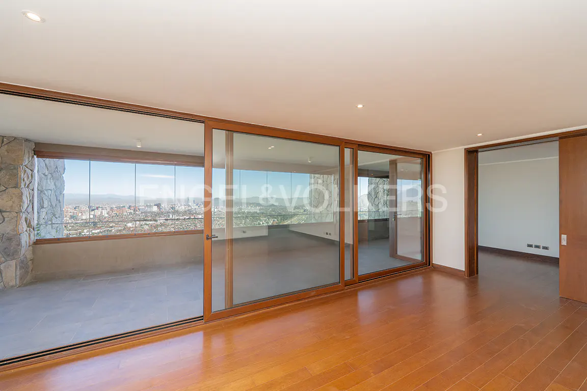 A bright, empty room with wood floors and large sliding glass doors to a balcony with a city view.