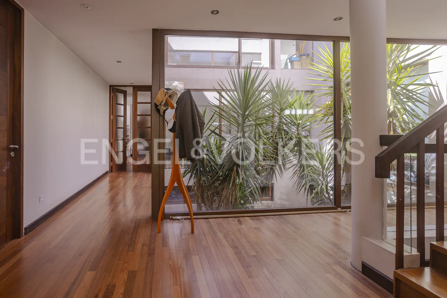 Bright hallway with wood floors, a coat rack with a jacket, and a large window with plants outside.