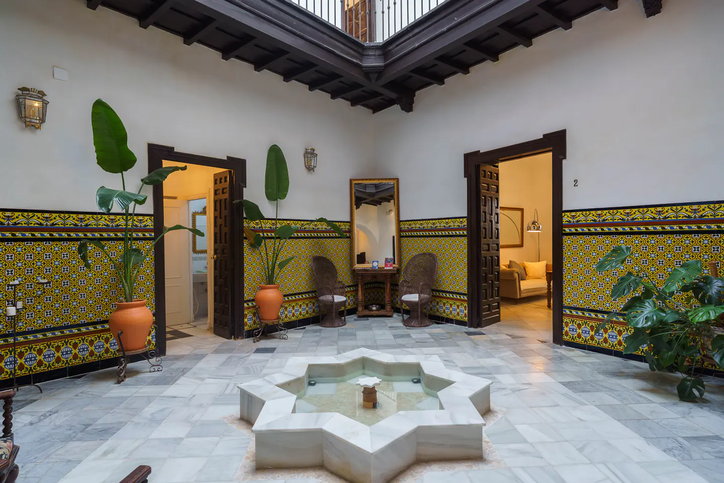 Interior courtyard with marble floors, a star-shaped fountain, potted plants, and yellow-patterned tile walls.