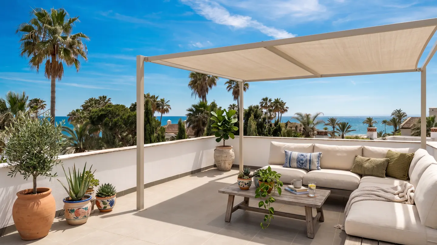 Rooftop patio with beige sofa, wooden table, and potted plants under a canopy. Palm trees and ocean view in the background.