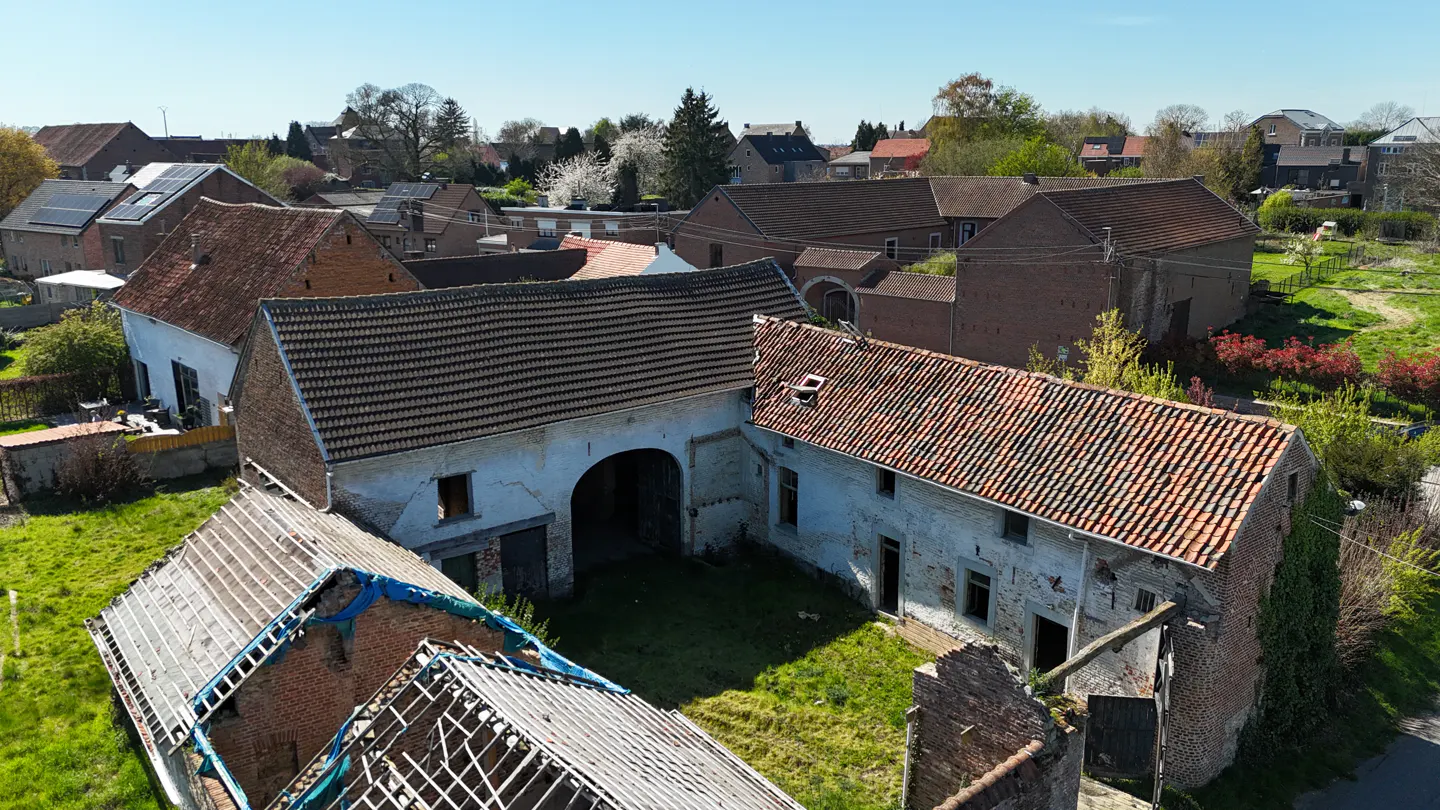 Aerial view of a rural property with brick and white buildings, some in disrepair, with tiled roofs and green grass.