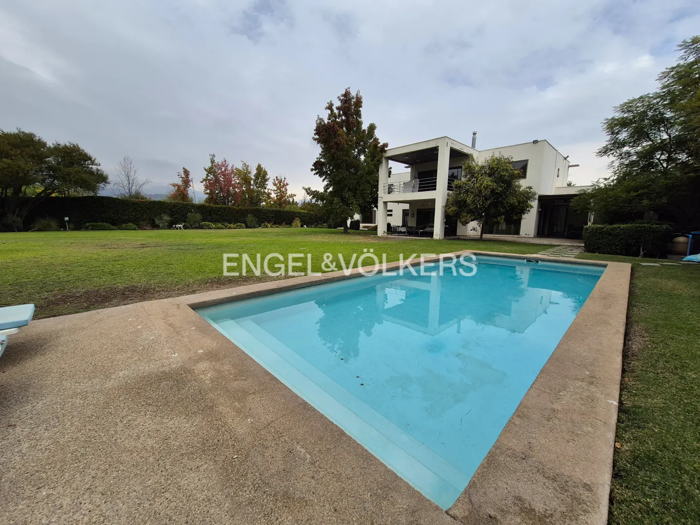 A rectangular swimming pool with blue water in front of a modern white house and green lawn.