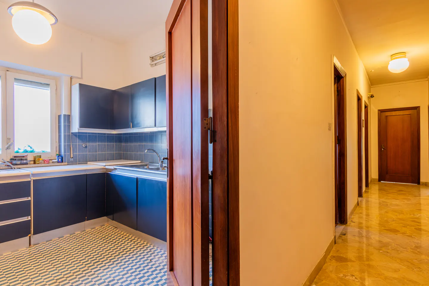 A view of a kitchen with blue cabinets and a hallway with wooden doors.