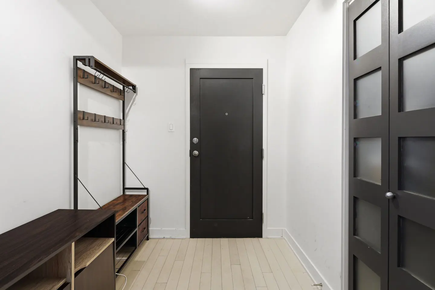 Entryway with a dark wood storage bench and coat rack, a black front door, and a closet with frosted glass panels.