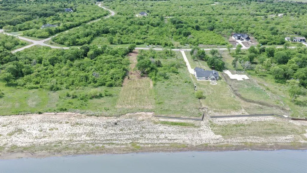 Aerial view of a waterfront property with a house, green trees, and a lake.