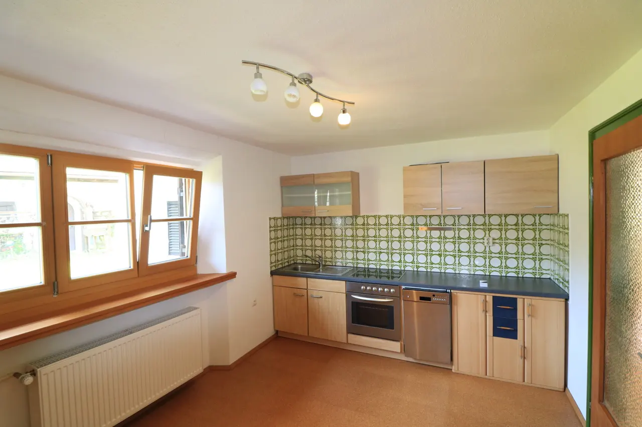 A bright kitchen with wood cabinets, green patterned backsplash, and a large window.