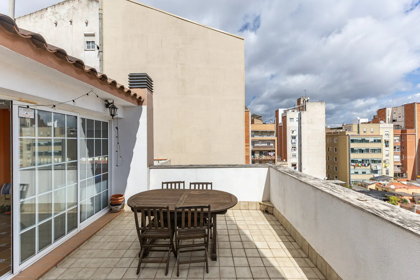 A rooftop patio with a dark wood table and chairs, white walls, and city views.