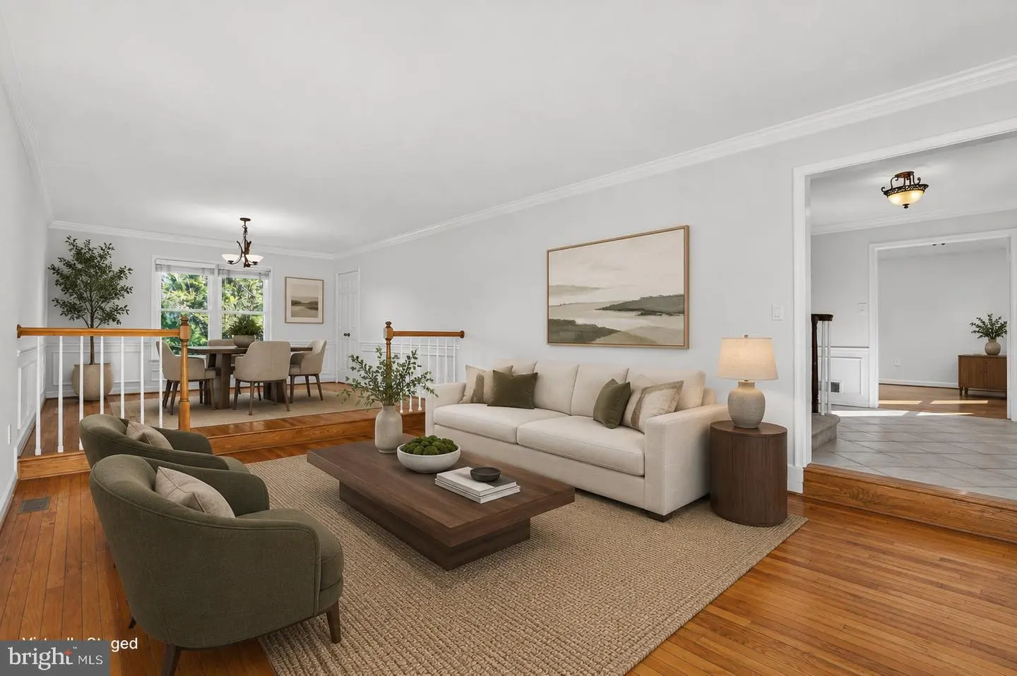 Bright living room with a beige sofa, two olive armchairs, a wooden coffee table, and a raised dining area with wood floors.