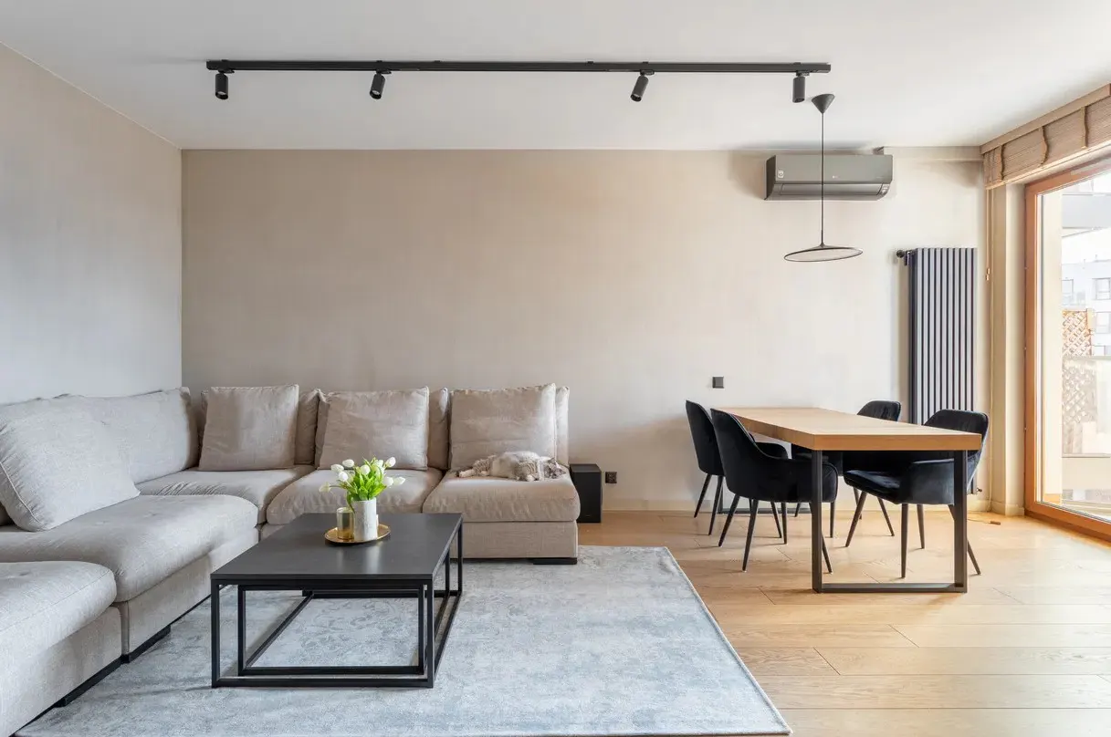 Living room with beige sectional sofa, black coffee table with tulips, wood dining table with black chairs, and light wood floors.