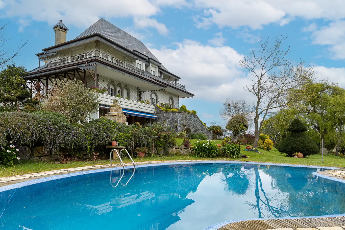 A large blue swimming pool in front of a white two-story house with a gray roof.