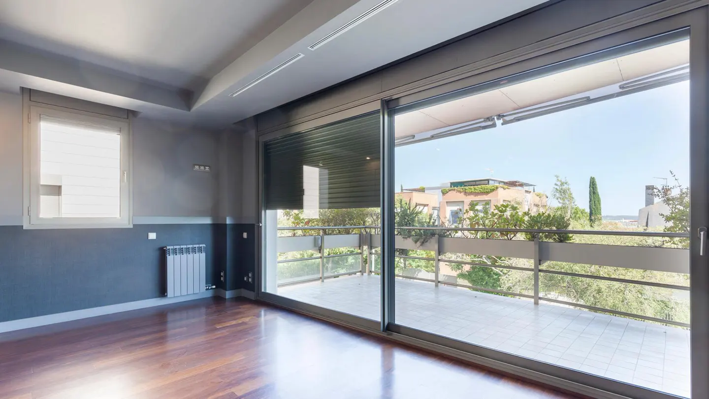 Empty room with dark wood floors, gray walls, and large sliding glass doors to a balcony with a city view.