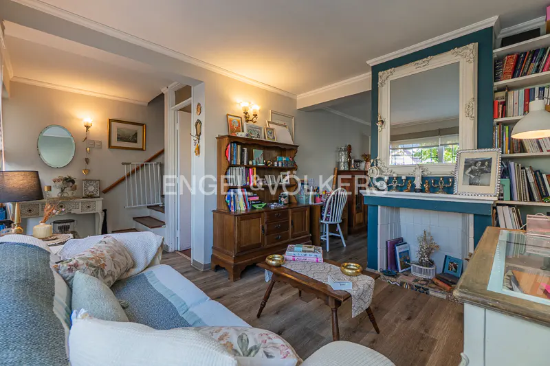A living room with a sofa, wooden floors, a fireplace with a mirror, and a bookshelf.