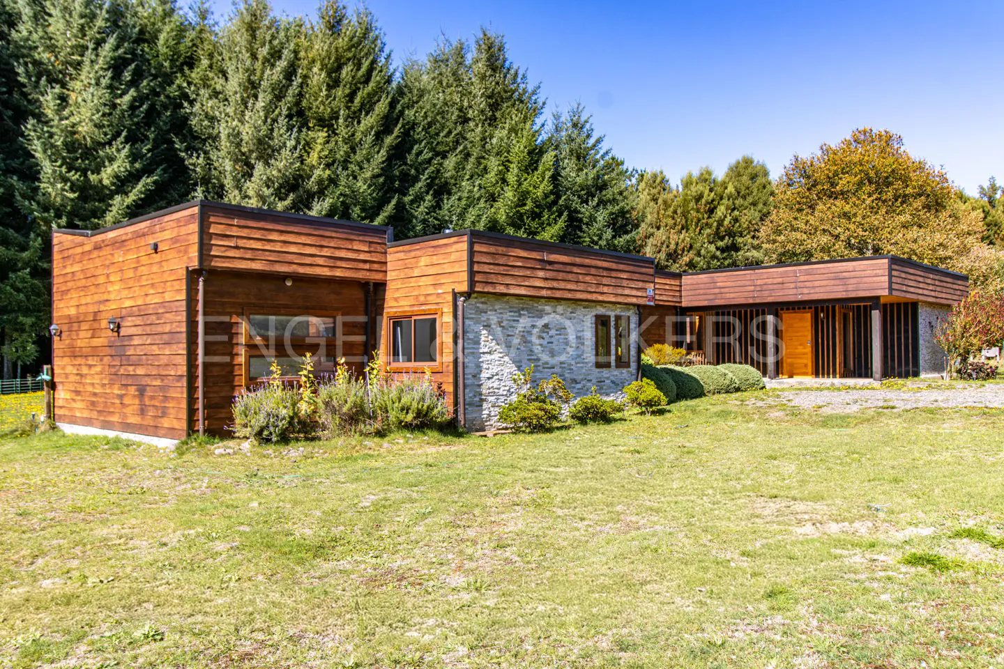 Modern home with wood and stone exterior, set on a green lawn with tall trees in the background.