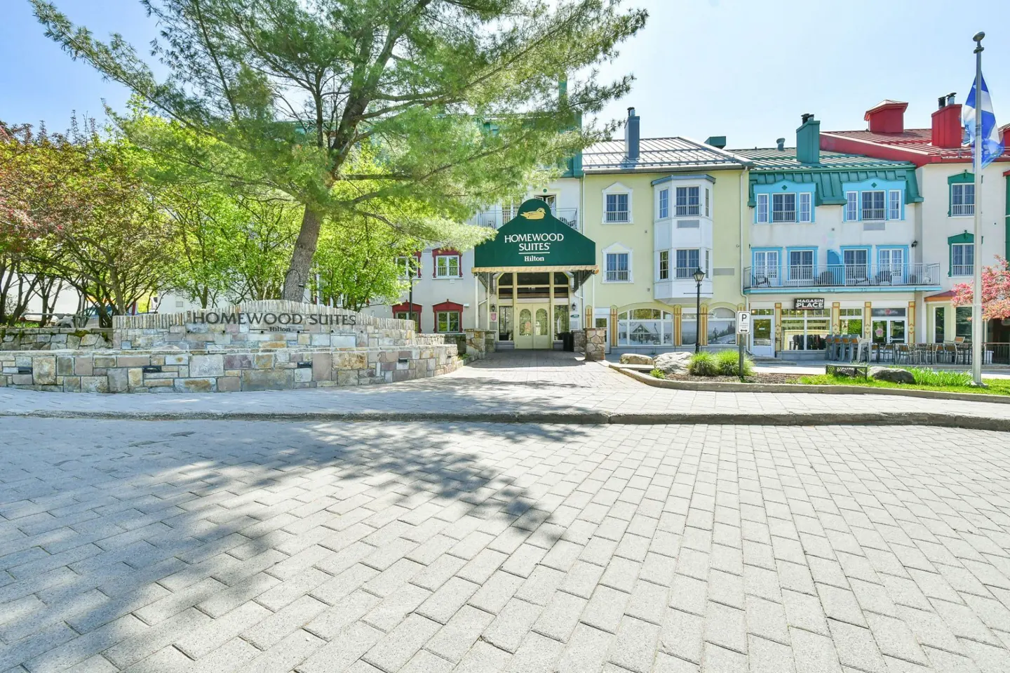 Homewood Suites hotel entrance with stone sign, green awning, and colorful buildings in the background.