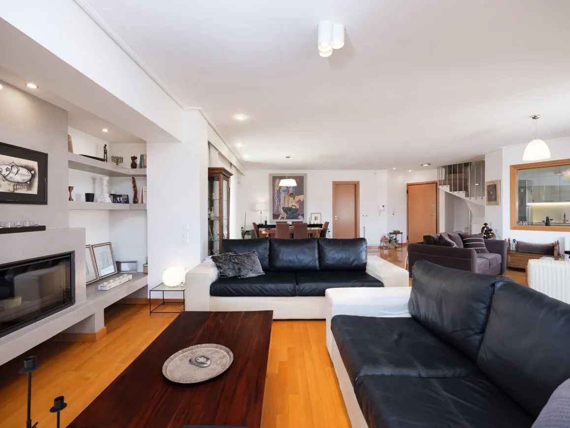 Bright, open-concept living room with hardwood floors, black and white sofas, a fireplace, and a dark wood coffee table.