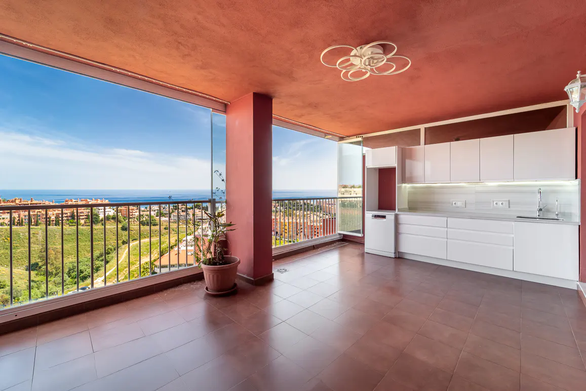Balcony with terracotta tile floor, red ceiling, white kitchen cabinets, and ocean view.