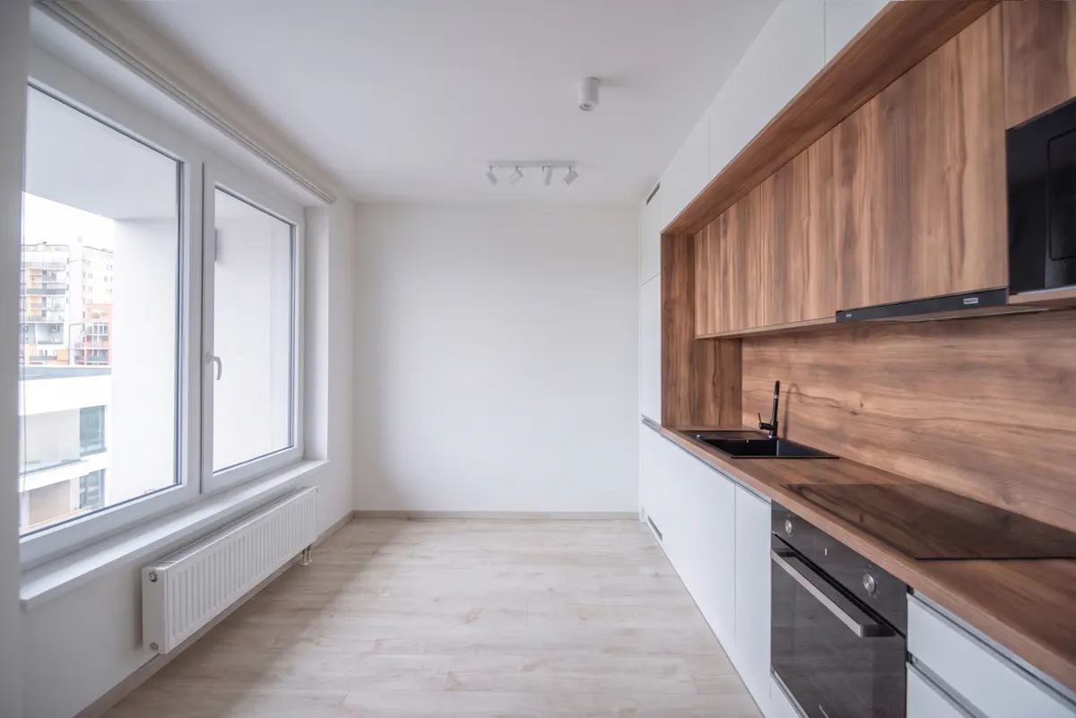 Modern kitchen with white walls, light wood flooring, and wood-grain cabinets featuring a black sink and built-in oven.