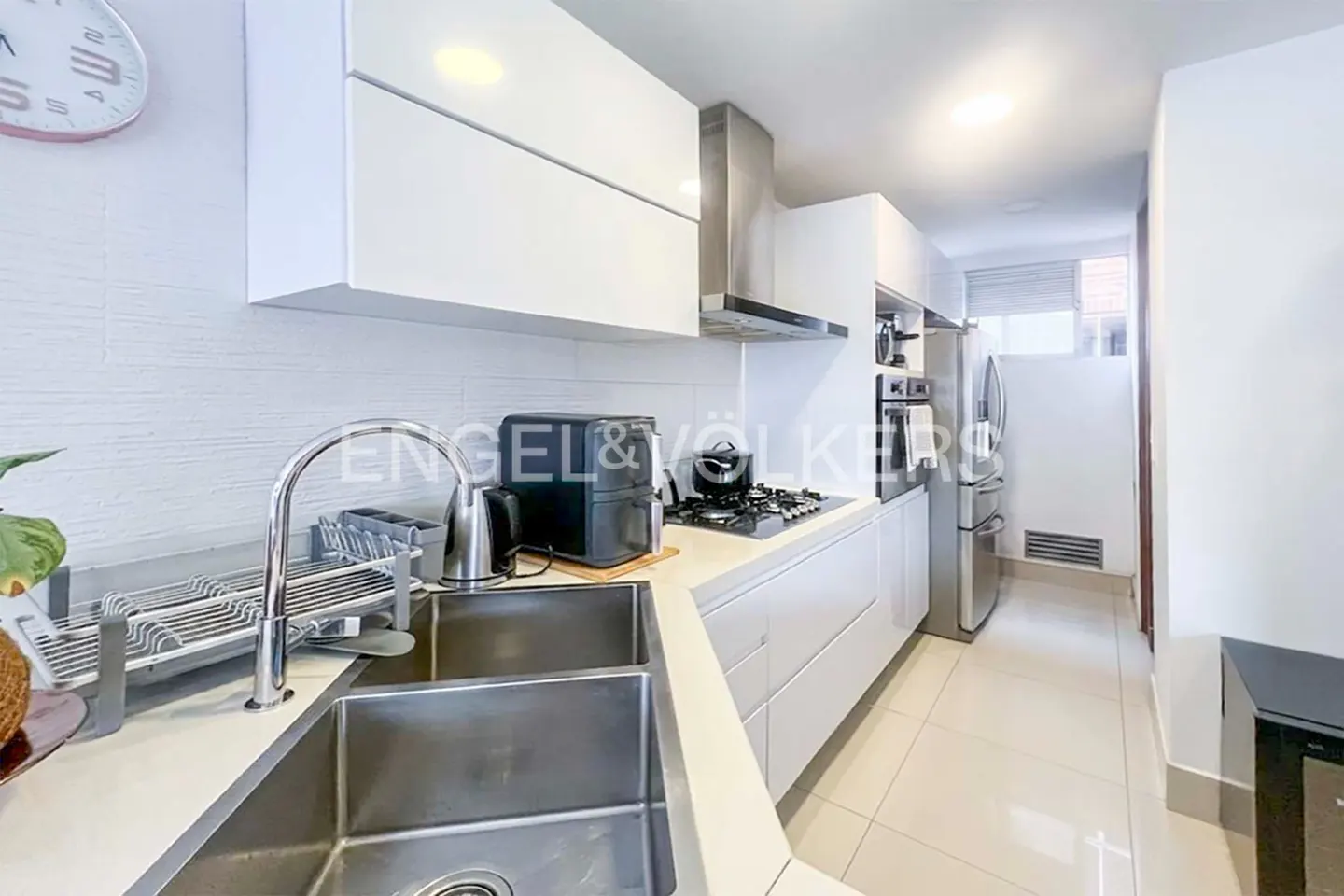 Bright kitchen with white cabinets, stainless steel appliances, and a double sink. A clock hangs on the wall.